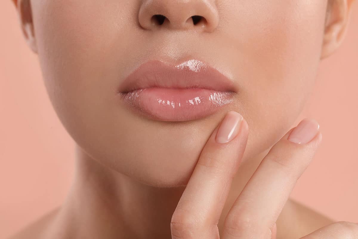 Young woman with beautiful full lips on peach background, closeu